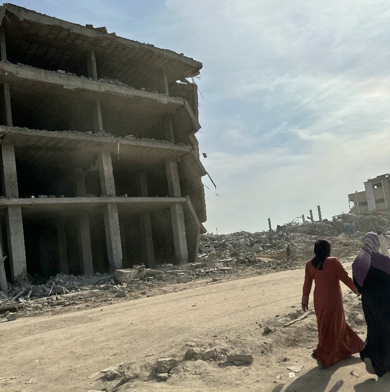 Two women walk by a ruined building in Gaza