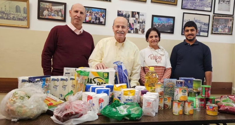 Munir Kakish and three colleagues stand behind a table of food provision and toiletries, including tins, meat and oil