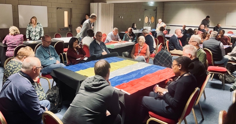 Members of Council sit around tables draped with flags of the countries they are praying for - including Russia and Uklraine