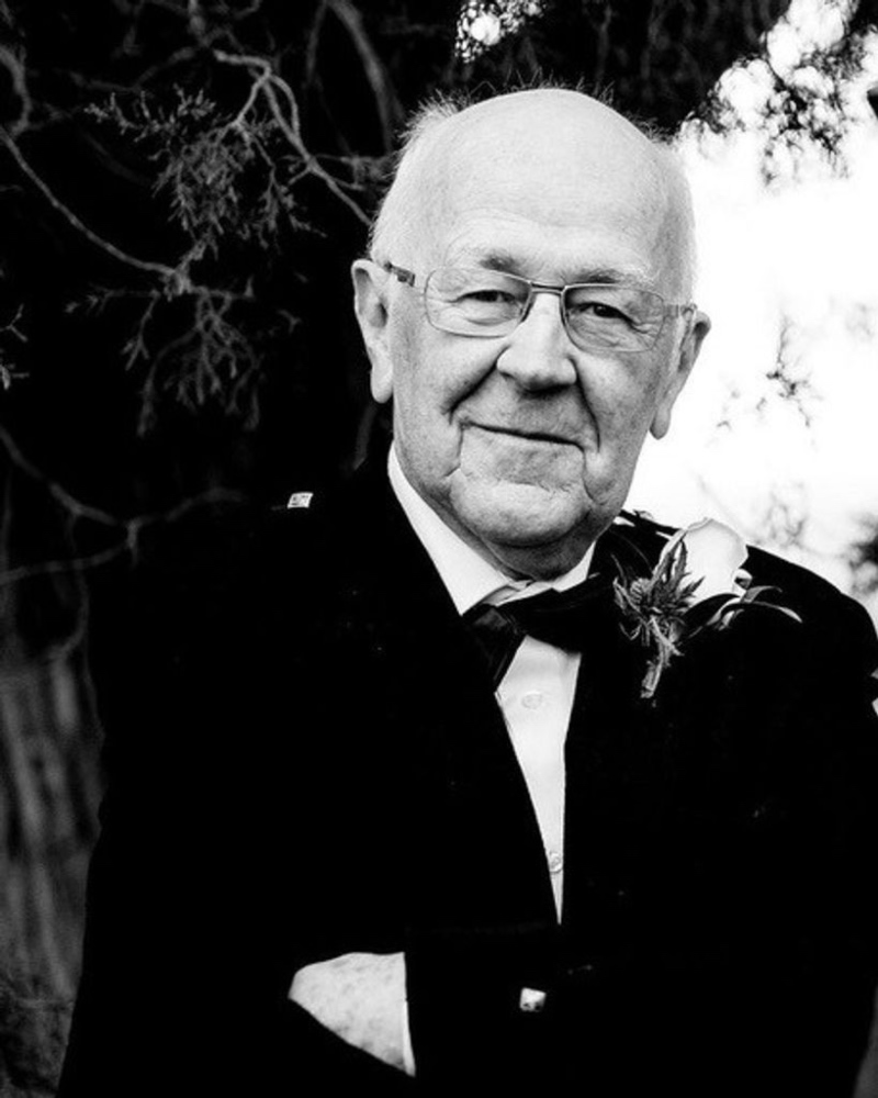 Black and white photo of Bruce Milne (1940-2025), in which he is wearing a ball suit and bow tie