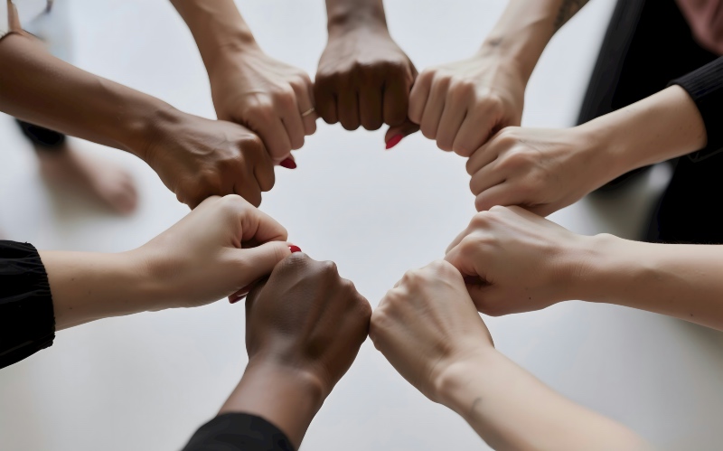 A top-down view of a diverse group of people forming a circle with their fists joined together in solidarity.
