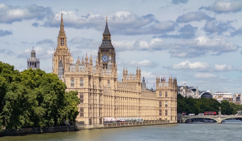A wide view of the Palace of Westminster and Elizabeth Tower (Big Ben) along the River Thames under a partly cloudy sky, with Westminster Bridge on the right.