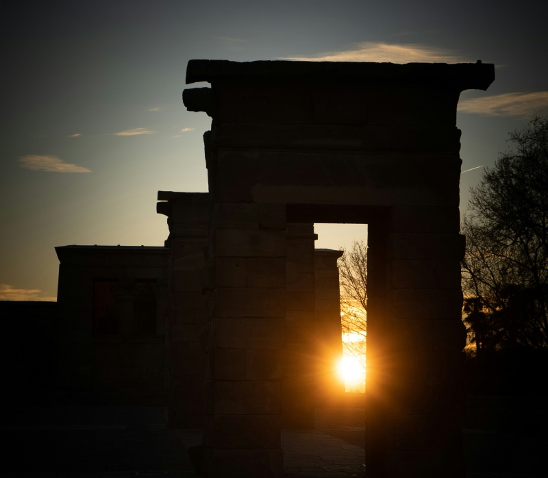 Silhouetted ancient stone archways with the setting sun shining brightly through one of the gateways